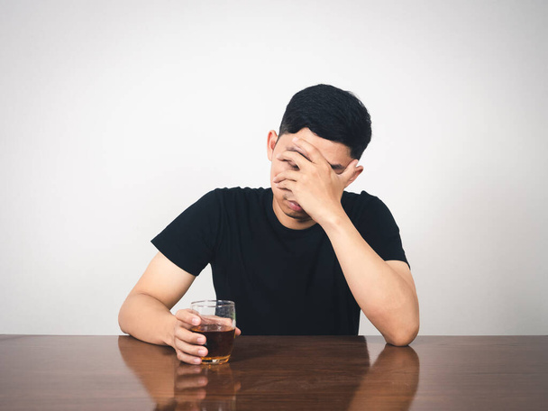 Depressed man sitting at table close his face and hold alcohol glass in hand - Photo, image