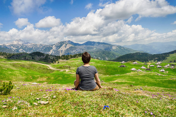 Woman enjoys views of the alpine village in the mountains. Velika Planina or Big Pasture Plateau in the Kamnik Alps, Slovenia. Mountain cottage hut or house. - 写真・画像