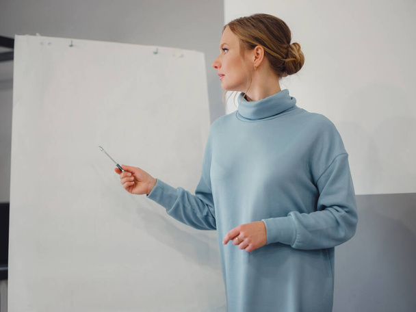Young female trainer or speaker making whiteboard presentation for employees in office, focused woman trainer presenting business project on flipchart at meeting. mock-up - Photo, Image
