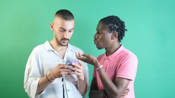 Twee mannelijke vrienden die één zwart zijn en de andere wit die samen naar de telefoon kijken, leuke dingen kijken aan de telefoon, beeld van emoties en gezichtsuitdrukkingen genomen voor het groene scherm - Video