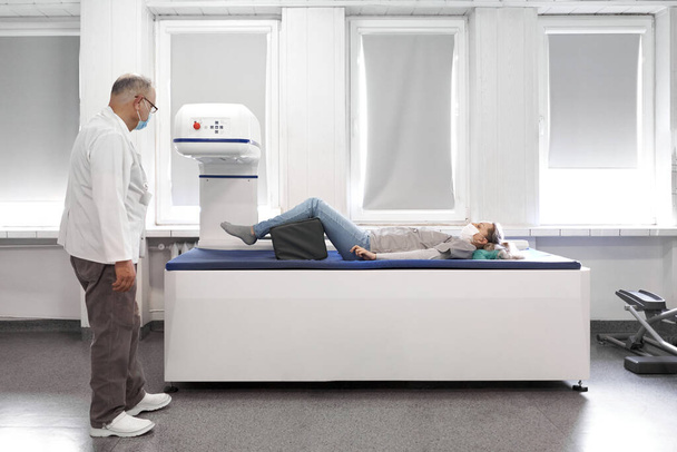 Female patient lying on a stretcher of a x-ray machine next to a female doctor with mask - Photo, image