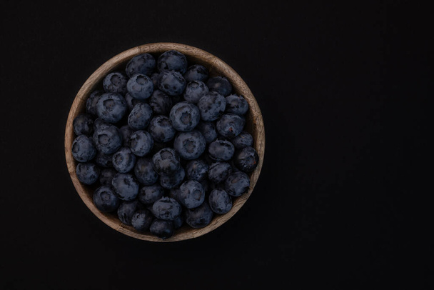 fresh blueberries with green leaf in wooden bowl isolated on black background, top view - Photo, image