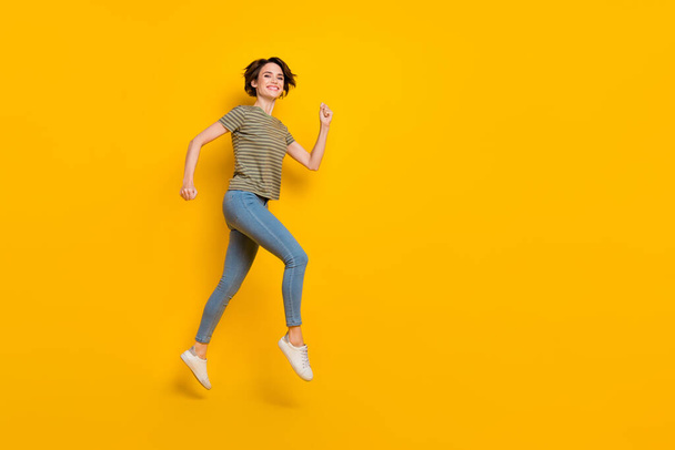 Full length photo of excited pretty girl dressed green t-shirt jumping high running empty space isolated yellow color background. - Фото, изображение