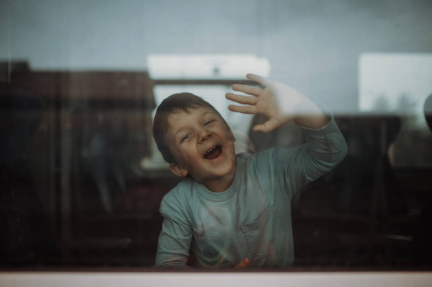 A happy little boy waving through window to say goodbye when travelling in train. - Foto, imagen