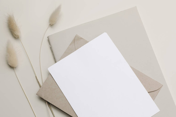 Closeup of empty paper greeting card, invitation and diary mockup. Boho stationery still life. Lagurus ovatus, bunny tail grassy foliage. Craft envelope. Beige table background, neutral top view. - Foto, Imagen