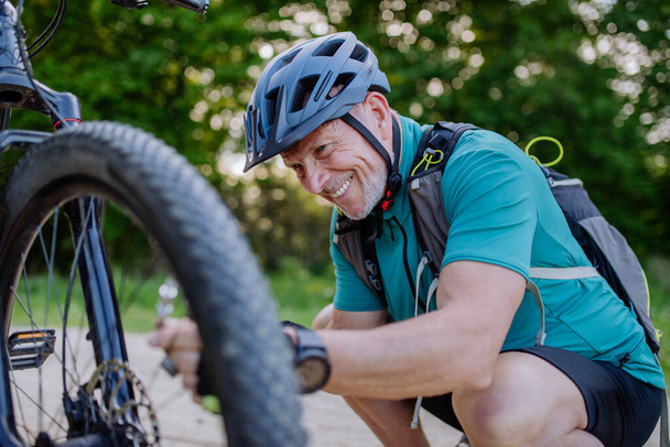 An active senior man repairing bicycle, pumping up tire in nature in summer. - Foto, Bild