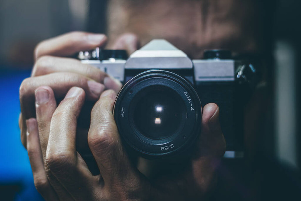Een man die een foto neemt met een oude filmcamera. Focus op de lens, close-up. - Foto, afbeelding
