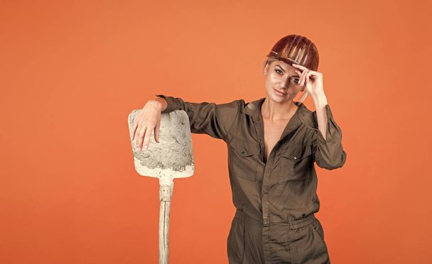 woman engineer in protective helmet and boilersuit hold shovel on orange background, industry. - Foto, immagini