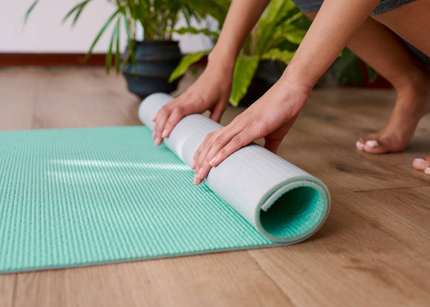 A young multi-ethnic woman rolls up her yoga mat at the end of her practice. High quality photo - Foto, immagini
