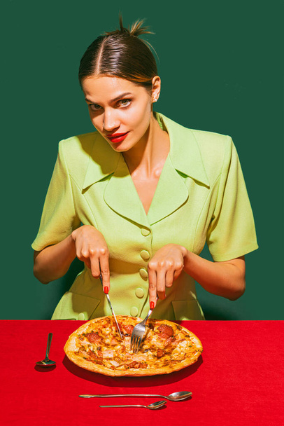 Young woman eating delicious Italian pizza isolated over green background. Traditional italian meal. Food pop art photography. Vintage, retro style. Complementary colors, Copy space for ad, text - Photo, image
