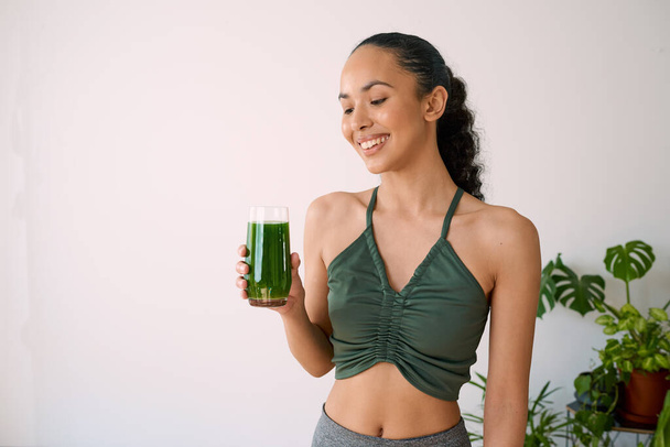 A beautiful multi-ethnic woman smiles with green juice - spinach, kale, vitamans. High quality photo - Foto, Imagem