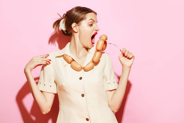 Young woman emotionally eating sausage on her necklace Creative food advertisement. Food addiction. Food pop art photography. Vintage, retro style. Complementary colors, Copy space for ad, text - Фото, изображение