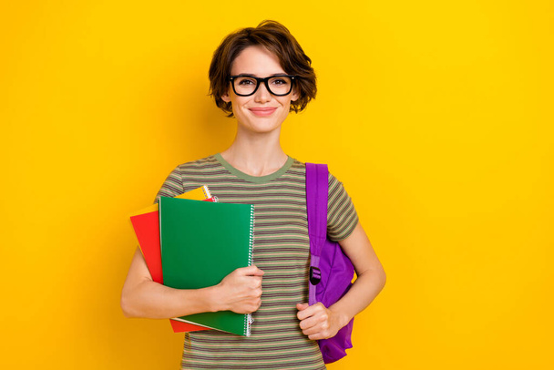 Photo of sweet cheerful girl dressed green t-shirt eyewear rucksack holding book isolated yellow color background. - 写真・画像