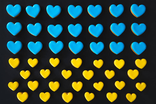 Żółte i niebieskie ręcznie robione pierniki w kształcie serc na czarnym tle, płaskie układanki, flaga Ukrainy koncepcja, bez wojny. - Zdjęcie, obraz