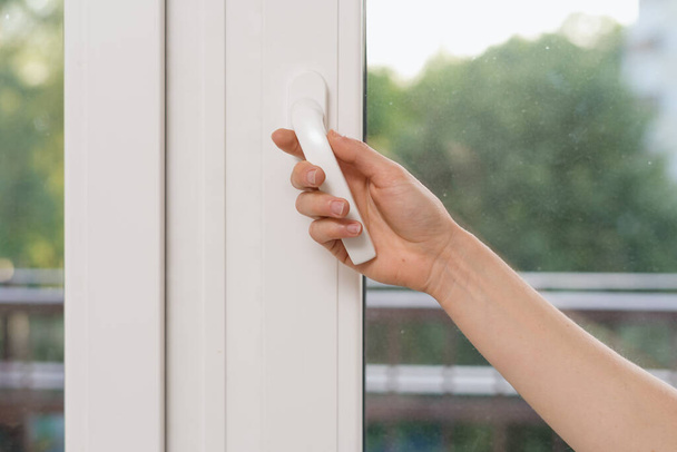 Cropped view of woman hand open plastic window in living room. Female hold handle, closed double glazed pvc balcony door, protect bedroom and insulate apartment from outdoors noise - Foto, imagen