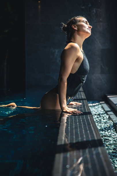 Vonzó fiatal nő fekete fürdőruhában pihentető a medencében a spa komplexum. - Fotó, kép