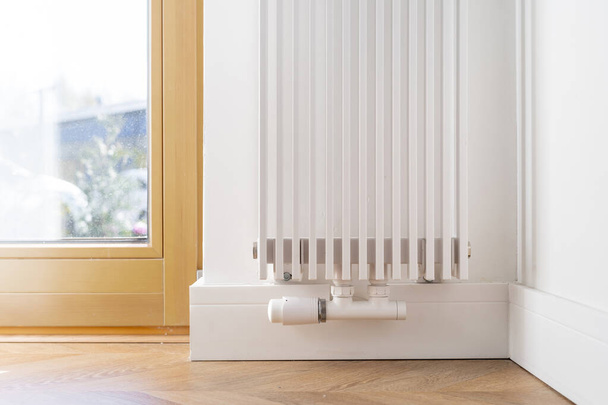 Oříznutý pohled na bílý stylový chladič v současném obývacím pokoji s dřevěnou podlahou. Spotřeba energie. Zařízení ústředního vytápění. Proces přenosu tepla - Fotografie, Obrázek