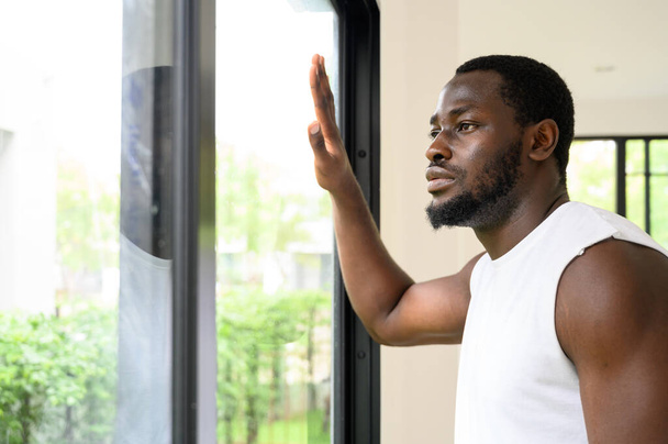 Портрет задумчивого афроамериканца, стоящего, трогательного и смотрящего в окно дома - Фото, изображение