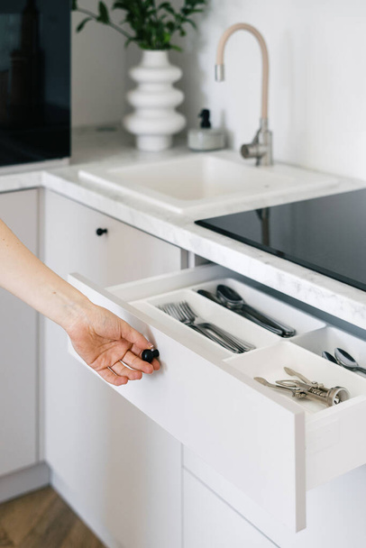 Cropped view of woman open white cutlery drawer in a modern apartment. Housewife holding clean shiny silverware in box with separate sections. Concept organization of space at kitchen - Foto, immagini