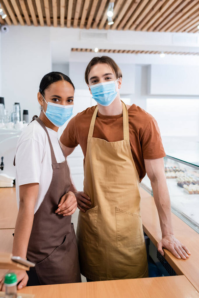 Interracial sellers in medical masks looking at camera in confectionery  - Φωτογραφία, εικόνα