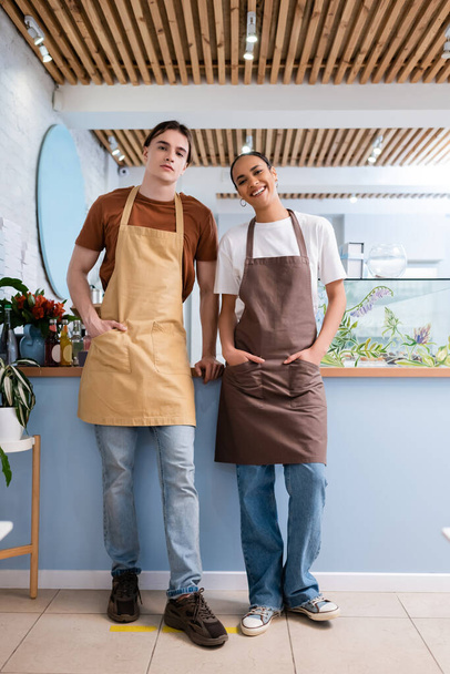 Multiethnic sellers in aprons looking at camera in confectionery  - Foto, Imagen