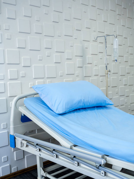 Empty patient bed in a hospital room with blue pillow and bedsheet on white wall background, vertical style. Sick bed in recovery room with electric adjustable background, Health care medical concept. - Photo, image