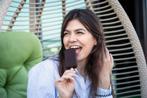 Happy young woman with chocolate ice cream, sundae, popsicle in a hammock on the terrace. - Fotoğraf, Görsel