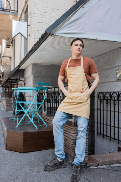 Smiling salesman in apron standing on terrace of confectionery outdoors  - Фото, зображення
