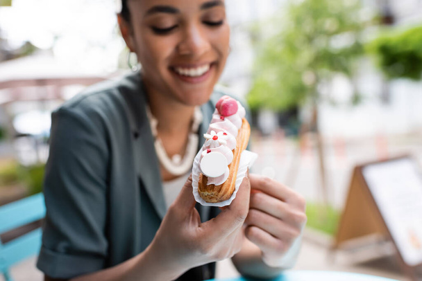 Cheerful african american woman holding eclair with cream outdoors  - Фото, зображення