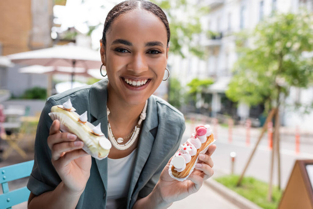 Positive afrikanisch-amerikanische Frau hält köstliche Eclairs auf der Süßwarenterrasse  - Foto, Bild