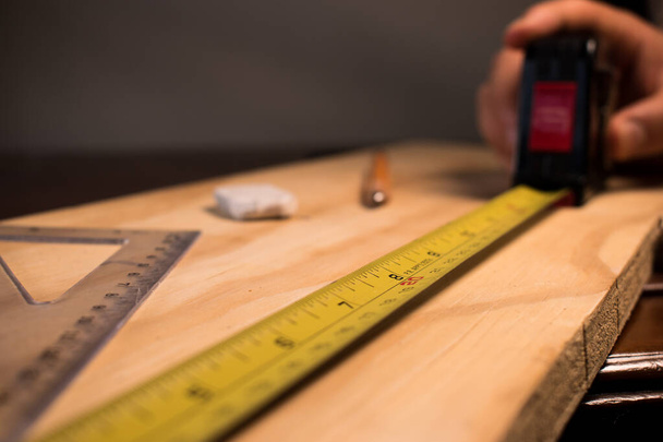 Carpenter taking wooden table measurements with some tools - Фото, изображение