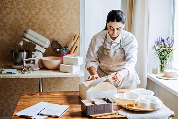 Female baker, pastry chef preparing cake order. Arabic Asian woman making cake for online selling delivery. Female small business bakery shop owner preparing order for customer. - Фото, зображення