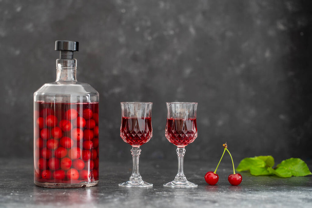 Homemade cherry brandy in two glasses and in a glass bottle on a black background, close up - Valokuva, kuva