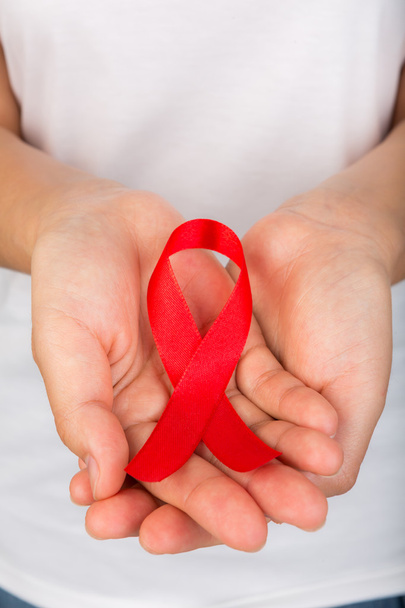 Female hands holding red AIDS awareness ribbon - 写真・画像