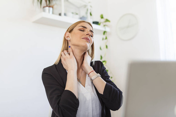 Feeling exhausted. Frustrated young woman looking exhausted and massaging her neck while sitting at her working place - Foto, Bild