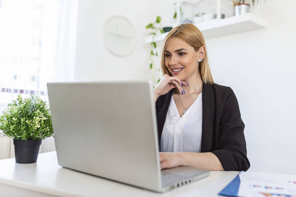 Portrait of happy young woman looking at laptop working at home. Successful lady laughing and working at home. Beautiful stylish woman smiling and working at home. - Фото, изображение