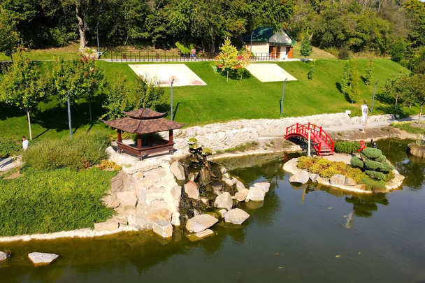 A beautiful Japanese-style landscape park in New Sofiyivka. Lake, wooden arbors, red bridge, Aerial view from drone on park. Uman, Ukraine, 2021-09-12 - Photo, image