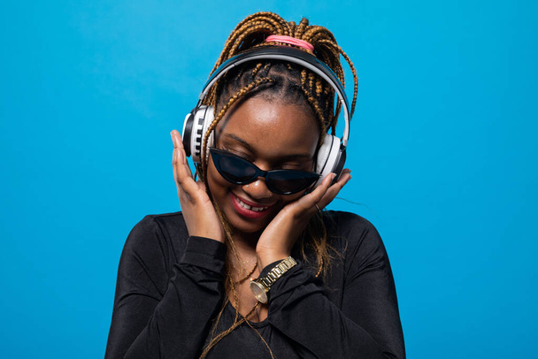 A contented dark-skinned girl listens to music on wireless headphones. Slightly tilted head. Focused while listening to music. - Fotoğraf, Görsel