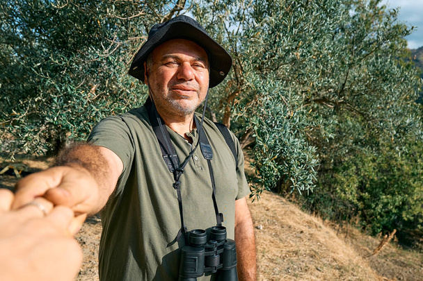Proszę za mną. Brodaty mężczyzna chwycił i pociągnął za rękę fotografa prowadząc ją po gaju oliwnym w górach. Pojęcie wspólnoty i beztroskiego nowoczesnego życia, zdrowego stylu życia, sportu i trekkingu. - Zdjęcie, obraz
