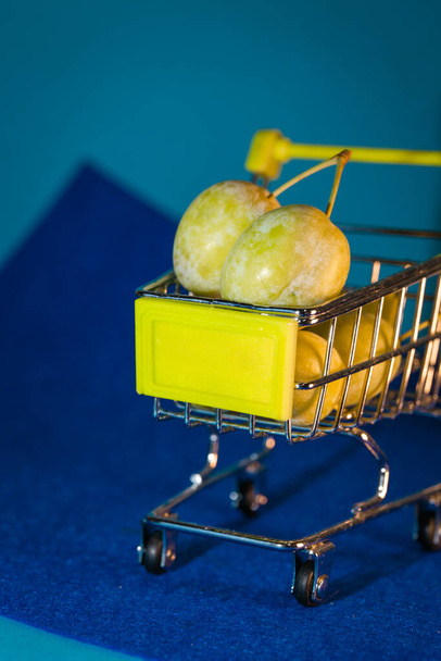 plums in a small supermarket cart on a blue background. - 写真・画像