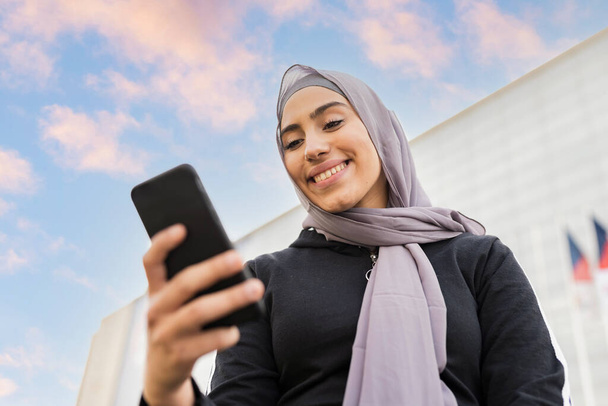 Muslim woman in hijab uses smartphone while communicating with friends and smiling - Photo, image