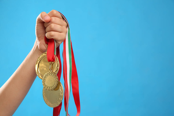 Woman holding gold medals on light blue background, closeup. Space for text - Foto, immagini