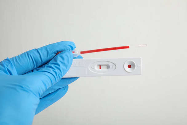 Doctor holding disposable express test for hepatitis and pipette with blood on white background, closeup - Fotoğraf, Görsel