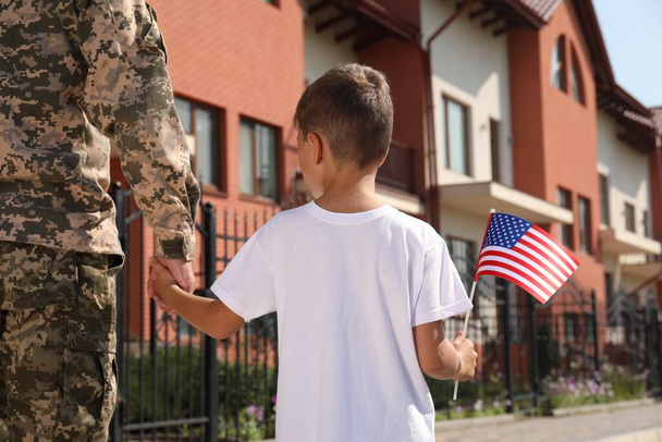 Soldier and his little son with American flag outdoors, back view. Veterans Day in USA - Foto, afbeelding