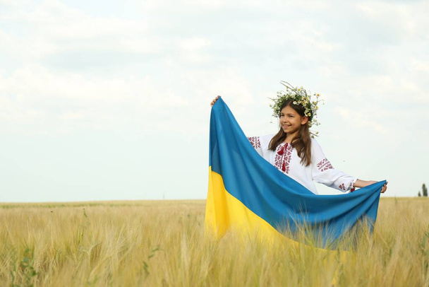 Happy little girl with national flag of Ukraine in wheat field. Space for text - Valokuva, kuva