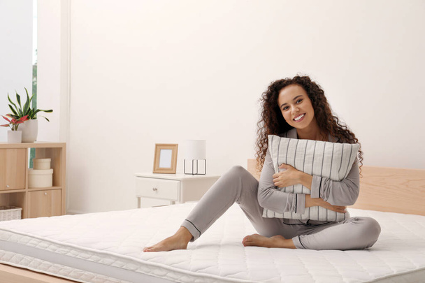 Happy young African American woman hugging pillow on bed with comfortable mattress at home - Foto, Imagen