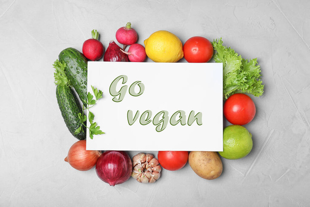 Paper card with phrase Go Vegan and fresh vegetables on light grey background, flat lay - Fotó, kép