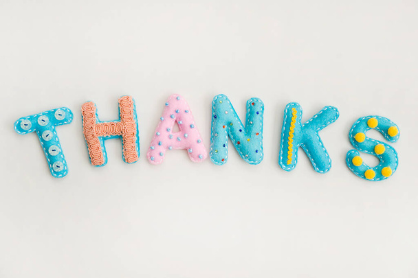 Stuffed felt letters with decorations. Word "Thanks" on isolated neutral background. Handmade crafts. Flat lay. - 写真・画像