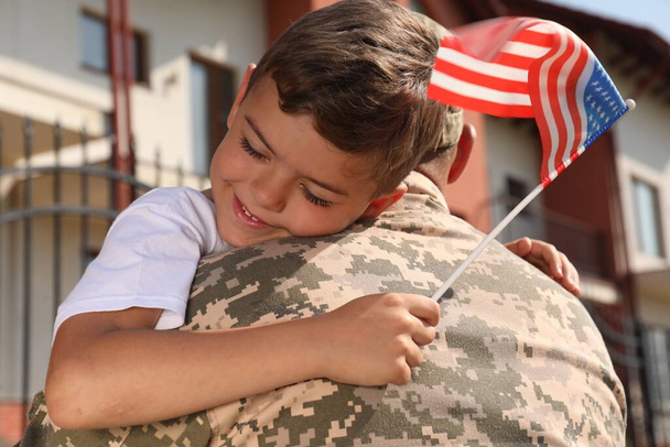Soldier and his little son with flag of USA hugging outdoors - Foto, afbeelding