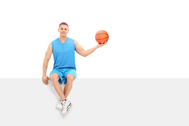 Basketball player sitting on blank billboard - Фото, изображение